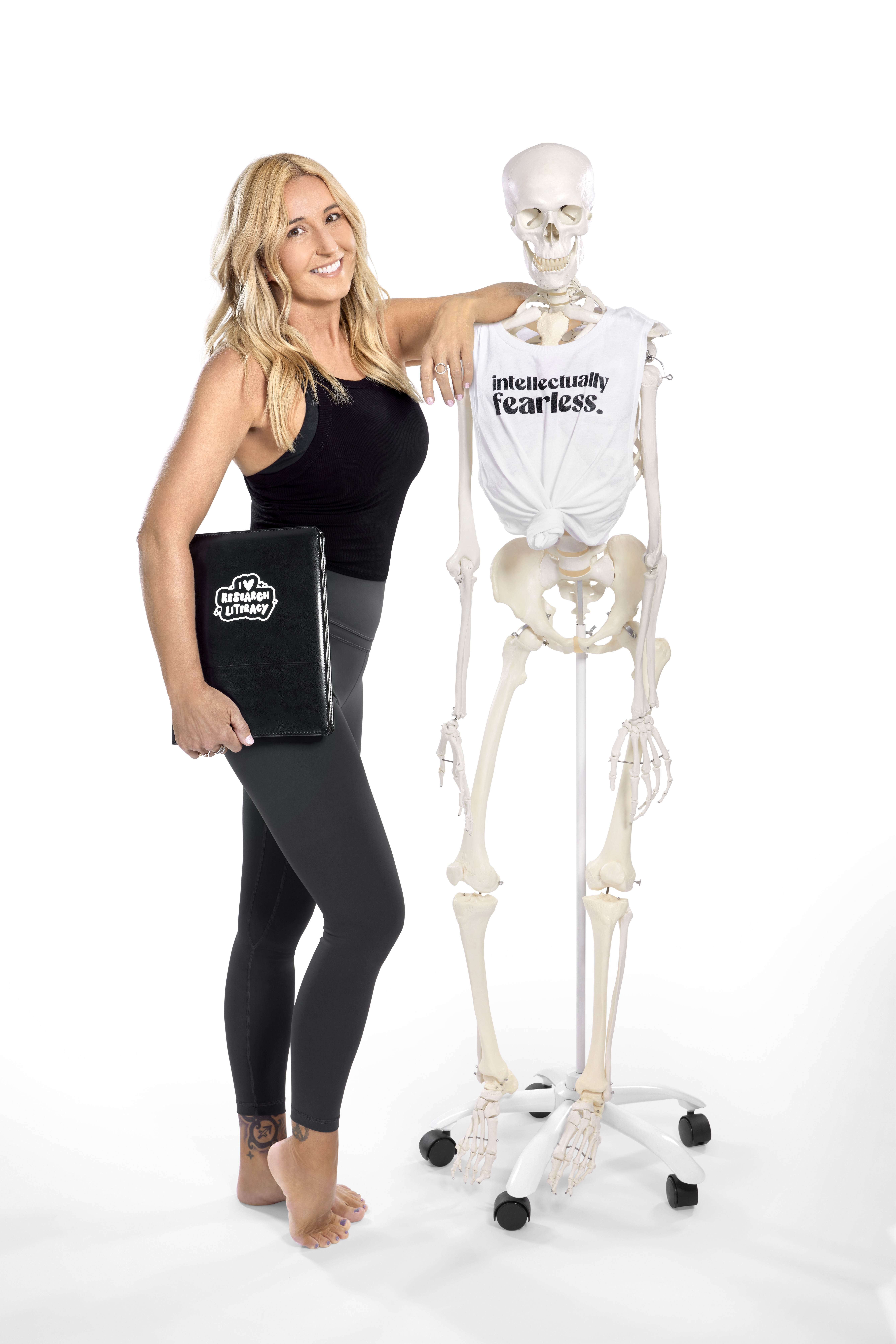 Jules Mitchell posing with a skeleton wearing a shirt that says "intellectually fearless" and holding a notebook with an "I love research literacy" logo on it.